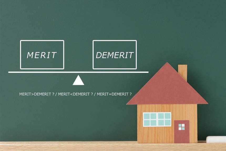「MERIT」「DEMERIT」が書かれた黒板の前にある家の模型